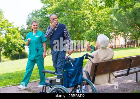 Ein älterer Mann mit der Krankenschwester auf einem Spaziergang durch den Garten eines Pflegeheims, der eine ältere Frau begrüßt Stockfoto