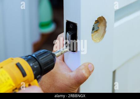 Mit Hilfe eines Schraubendrehers schließt der Arbeiter die Montage des Schlosses an der Innentür ab. Stockfoto