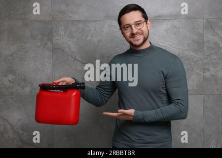 Ein hübscher Mann, der einen roten Kanister an der grauen Wand zeigt Stockfoto