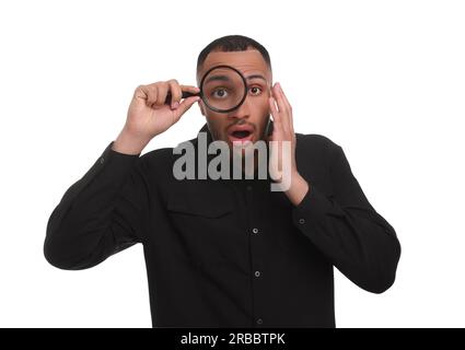 Schockierter Mann, der durch eine Lupe auf weißem Hintergrund blickt Stockfoto