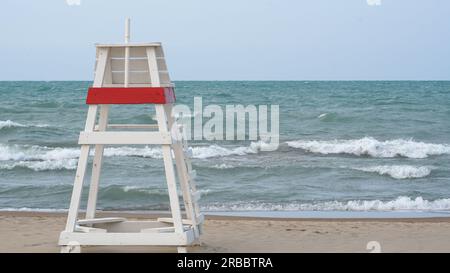 Leerer Rettungsschwimmer-Sessel mit Blick auf zerklüftete Gewässer am Lake Michigan, wenn das Wasser am Gillson Beach aufgrund von starkem Wind und hohen Strömen geschlossen ist. Stockfoto