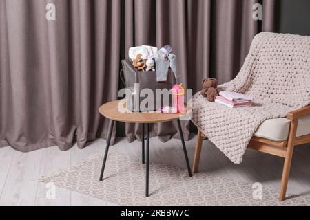 Muttertasche mit Babysachen auf Holztisch im Haus Stockfoto