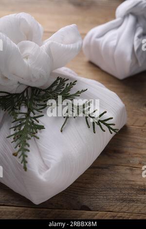 Furoshiki-Technik. Geschenke in weißem Stoff und Thuja-Äste auf Holztisch Stockfoto