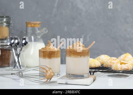 Gläser köstlichen Dalgona-Kaffee und Schneebesen auf dem weißen Tisch Stockfoto