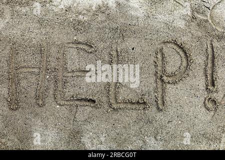 Das Wort hilft im Sand am Strand geschrieben. Das Konzept eines Hilferufens. Ein Wort, handgeschrieben auf Sand Stockfoto