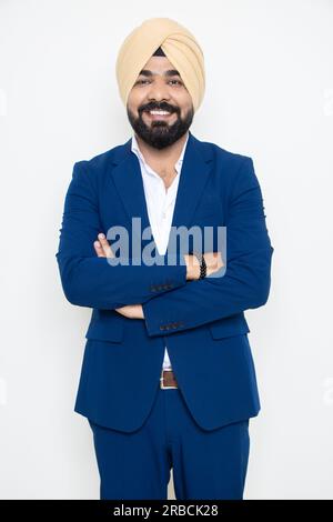 Ein glücklicher junger indischer sikh-Geschäftsmann, der einen Anzug trägt und im Armen steht, isoliert auf weißem Hintergrund. Unternehmenskonzept. Stockfoto