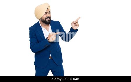 Ein glücklicher indischer sikh-Geschäftsmann, der einen Anzug trägt, der auf leere Räume zeigt, isoliert auf weißem Hintergrund. Hier, Werbung und Beförderung. Stockfoto