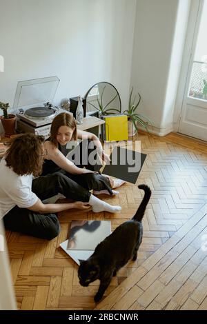 Ein junges Paar sitzt auf dem Boden und hört Musik auf einem Vinyl-Player mit verschiedenen Schallplatten Stockfoto