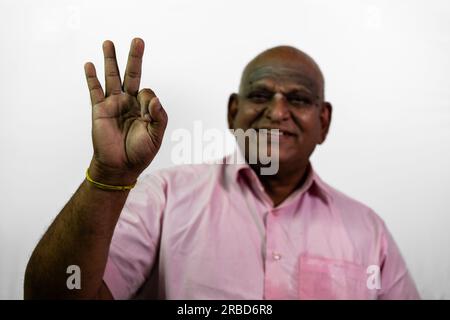 Ein südindischer alter Glatzkopf ist unscharf und sagt super vor der Kamera. Sein Finger ist auf einem weißen Hintergrund konzentriert. Stockfoto