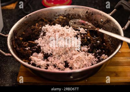 Nahaufnahme von Hammelfleisch und Blut, das in einer Pfanne mit Kokosmilch gebraten wird. Der Koch gibt mehr Kokosmilch in den Topf, und die Mischung ist Stockfoto