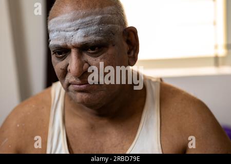 Ein trauriger, fetter Mann sitzt auf einem Bett und schaut nach unten. Stockfoto