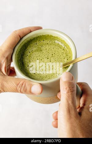 Draufsicht auf Matcha Latte: Eine verführerische Mischung aus grüner Perfektion, serviert mit einem goldenen Löffel inmitten von lebendigem grünem Pulver. Stockfoto