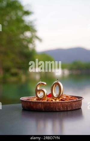 60-jähriger Mensch mit goldenen Kerzen auf einem Kuchen im See. Geburtstagsfeier eines erwachsenen Menschen Stockfoto