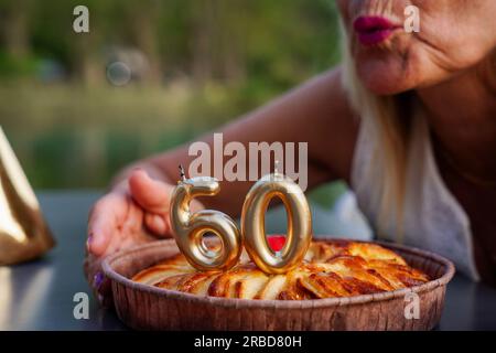 Reife Frau, die in 60 Jahren die Kerzen ausbläst. Geburtstagsfeier mit Kuchen Stockfoto