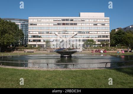 Medizinisches Personal, das sich neben Naum Gabos drehendem Torsionsbrunnen im St. Thomas' Hospital Courtyard, London, SE1, England, Großbritannien, entspannen kann Stockfoto