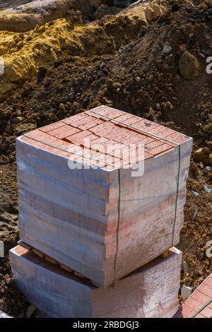 Paletten und Pakete mit roten Ziegeln in einem Baulager auf der Straße. Baumaterial roter Ziegel mit Löchern. Massive Tonziegel für Bausteine Stockfoto