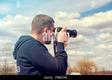 Person, die mit einer Reflexkamera fotografiert. Mann mit schwarzer Fotokamera an warmen Sommertagen Stockfoto
