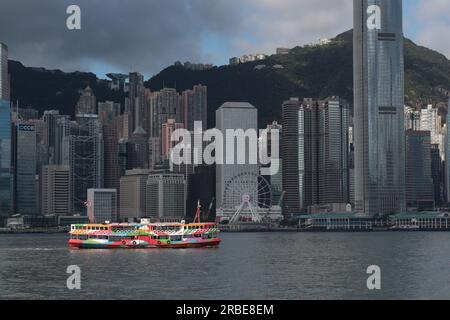 Blick auf die zentrale Uferpromenade (im Schatten) mit farbenfroher Star Ferry, die den Victoria Harbour überquert, von Tsim Sha Tsui, Kowloon, Hongkong, China Stockfoto
