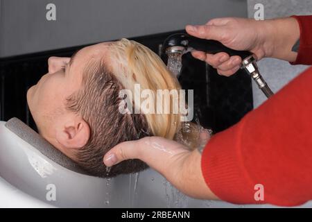 Die Hände des Friseurs gießen Regen und Wasser auf die Haare und den Kopf des Klienten des Kerls, bevor er im Friseursalon frisiert. Stockfoto