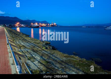 Küste des Hafens von Ushuaia bei Sonnenuntergang mit großen Schiffen mit angeschaltetem Licht Stockfoto