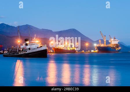 Küste des Hafens von Ushuaia bei Sonnenuntergang mit großen Schiffen mit angeschaltetem Licht Stockfoto