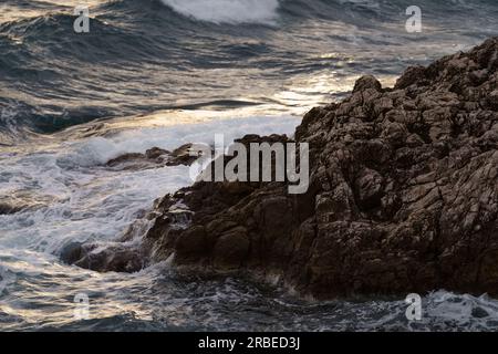 Meereswellen, die bei Sonnenuntergang gegen die Felsen der mittelmeerküste krachen, Reiseinhalt Stockfoto