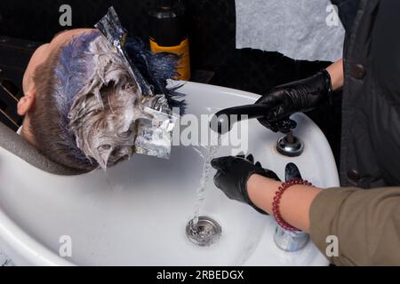 Die Hände eines professionellen Haarschneiders mit Handschuhen prüfen die Temperatur des Wassers, bevor sie die Haare des Klienten über dem Waschbecken waschen, bevor sie geschnitten werden Stockfoto