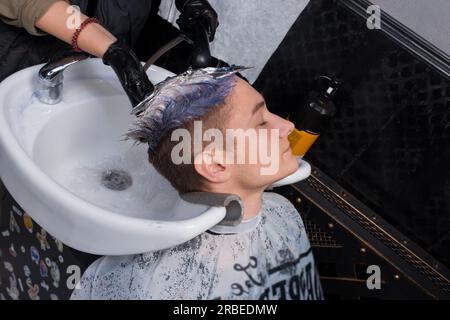 Junger attraktiver Friseurkundler, weiß, wäscht sich den Kopf über die Spüle, professionelle Dienstleistungen. Stockfoto