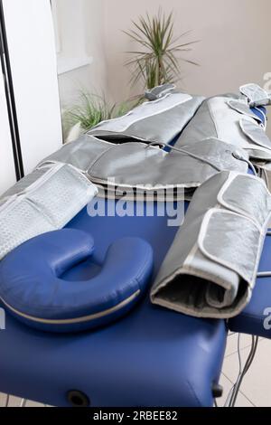 Drucktherapie grauer Massageanzug auf blauer Couch im Spa, Behandlung von Krampfadern, Ödem, Lymphdrainage, Gewichtsverlust. Entspannung Stockfoto