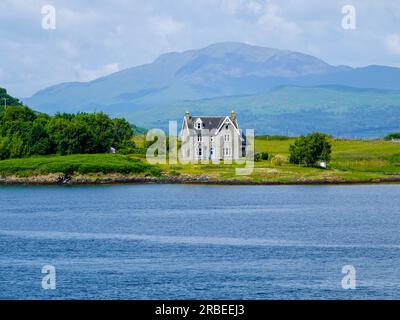 Haus am Ufer von Oban Bay mit Bergen im Hintergrund, Kerrera, Inner Hebrides, Schottland, Großbritannien. Stockfoto