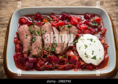 Hausgemachte Borschtsch-Suppe serviert mit gebratenen Wildscheiben aus einem Reh-Sattelfilet, serviert mit Creme Fraiche. England GB Stockfoto