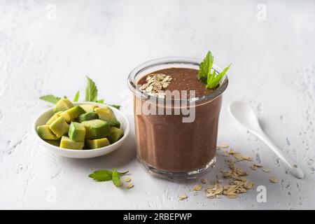 Schokoladen-Smoothie oder Cocktail mit gefrorener Avocado und Haferbrei garniert mit Minzblättern auf einem hellblauen Tisch. Veganes Essen Stockfoto