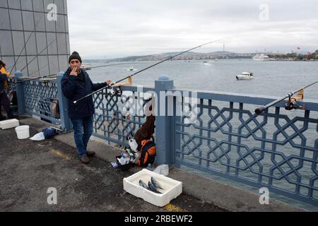 Ein türkischer Fischer wirft seine Angelrute und zeigt seinen Fisch auf der Galata-Brücke über das Goldene Horn und die Straße von Bosporus, Istanbul, Türkei. Stockfoto