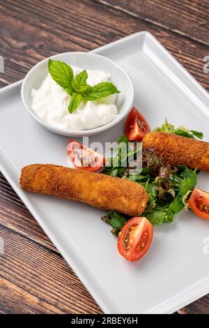 Mozzarella-Stäbchen mit Grün und Sauce auf einem weißen Porzellanteller Stockfoto