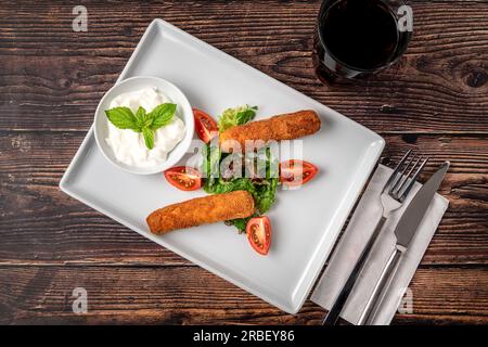 Mozzarella-Stäbchen mit Grün und Sauce auf einem weißen Porzellanteller Stockfoto