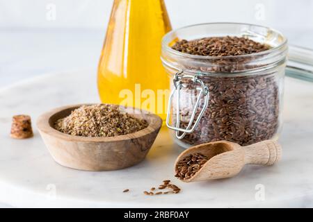 Eine Nahaufnahme von gemahlenen und ganzen Leinsamen mit Leinsamenöl dahinter. Stockfoto