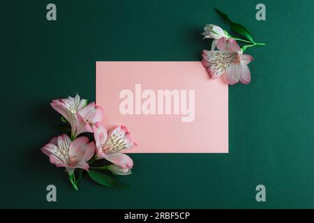 Wunderschöne Alstroemeria rosa Blumen und leere Karte auf dunkelgrünem Hintergrund, Modell. Draufsicht, flach liegend. Stockfoto