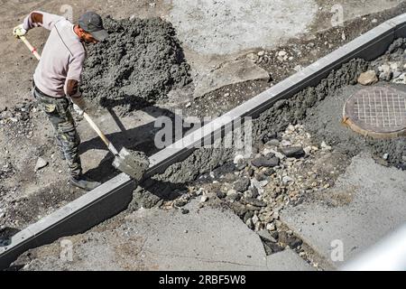 Legen von Bordsteinen auf der Straße oder auf der Straße am Sommertag. Der Baumeister gießt Zementsteine auf den Bürgersteig. Authentischer Workflow. Stockfoto