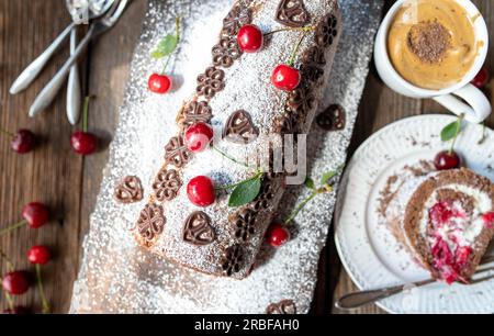 Schweizer Brötchen mit Sahne und Kirschen auf Holzhintergrund. Köstlicher Schokoladen-Kirschkuchen-Roulade Stockfoto