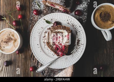 Eine Tasse Kaffee und Kuchen mit Kirschen auf einem Holztisch Stockfoto