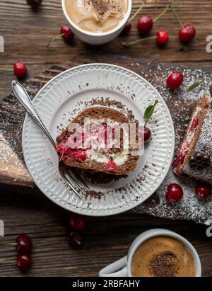 Ein Stück Schwarzwaldkuchen-Roulade auf einem Teller mit Holzhintergrund Stockfoto
