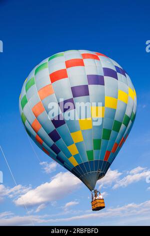 Wunderschöner farbenfroher Heißluftballon vor einem tiefen blauen Himmel und weiße Wolken, die im Morgenlicht fliegen. Stockfoto