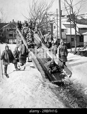 Rochester, New York: ca. 1911. Kinder, die in einer Freiluftschule in Rochester, New York, auf einer Holzrutsche rutschen. Stockfoto