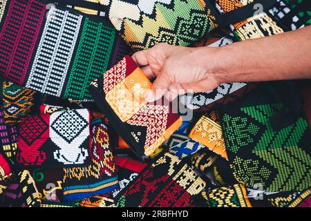 Eine Hand hält eine orangefarbene und rote Tasche oder eine Handtasche aus einem Haufen gemusterter Handtaschen. Selektiver Fokus. Nahaufnahme. Stockfoto