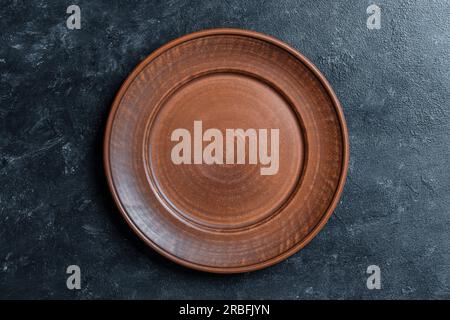 Leere flache Platte aus rotem Ton auf schwarzem Hintergrund. Draufsicht, Nahaufnahme. Grober Keramikhintergrund mit Kopierbereich Stockfoto