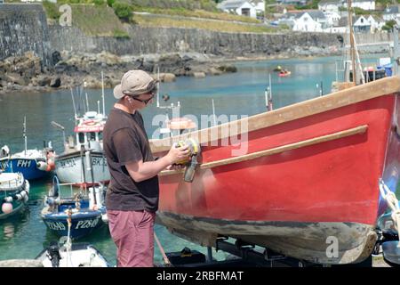 Coverack ist ein Fischerdorf am Meer auf der Eidechsenhalbinsel in Cornwall, Großbritannien. Ein junger Mann, der ein Boot am hafen von coverack wartet Stockfoto