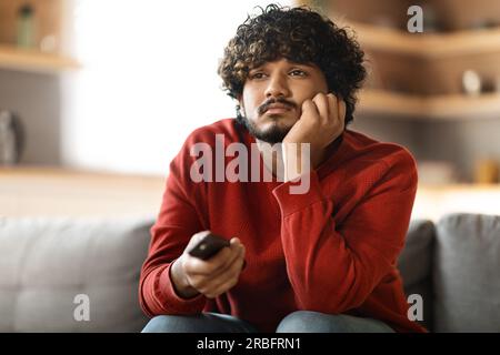 Porträt eines gelangweilten indianers, der zu Hause fernsieht und auf dem Sofa sitzt Stockfoto