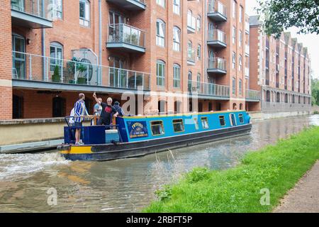 7 - 27-2019 Uhr Oxford England - Männer, die auf einem Flussboot an Apartments vorbeifahren, wobei ein Mann eine Schuljacke und Shorts trägt und ein anderer Stockfoto