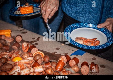 Shrimp und Crawdad Boil - Essen stapelt sich auf Papier, auf dem Tisch festgeklebt und Leute in der Schlange suchen sich aus, was sie wollen - Pappteller Stockfoto