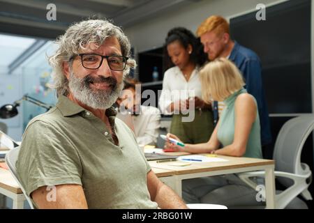 Porträt eines Büromanns, der lächelt und in die Kamera schaut. Im Hintergrund gibt es eine Gruppe von Menschen Stockfoto